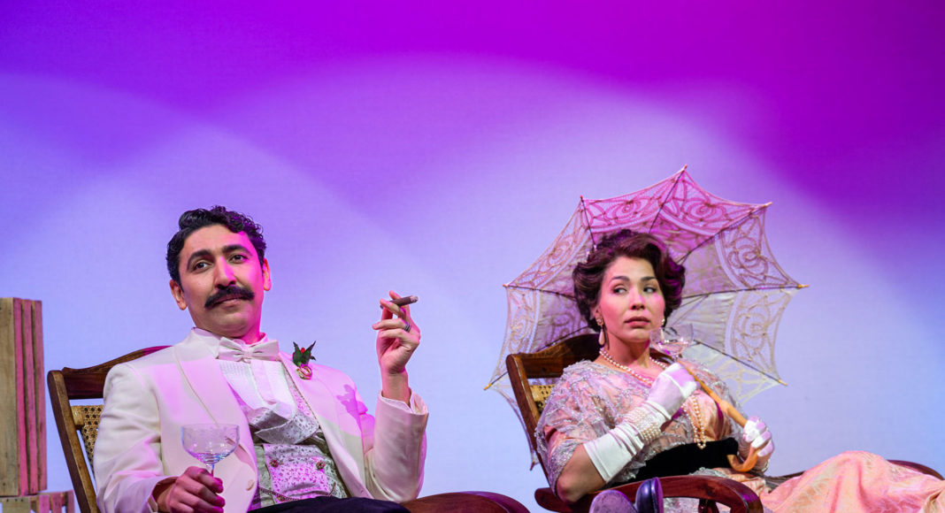 Two performers in Victorian costumes on a set with brightly colored background lights
