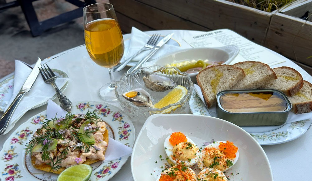 Table covered with white tablecloth, several plates of food and a glass of winewith several plates of