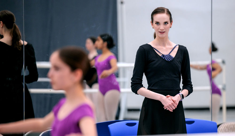 Ballerina in black leotard teaching a class of young dancers