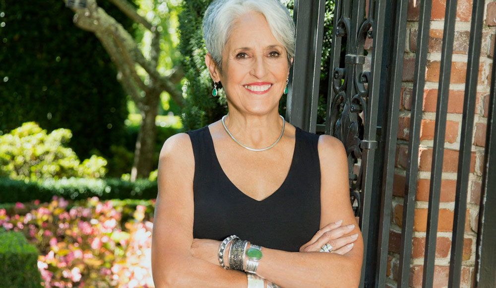 Smiling woman with close-cropped gray hair with her hands folded across her chest
