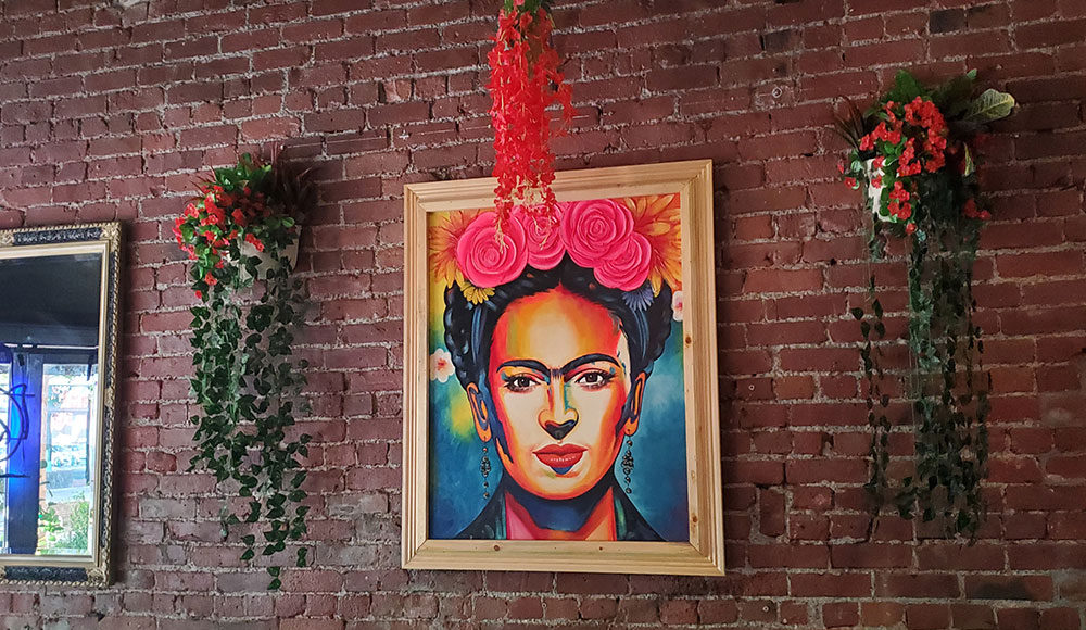 Framed illustration of Frida Kahlo hanging on a brick wall
