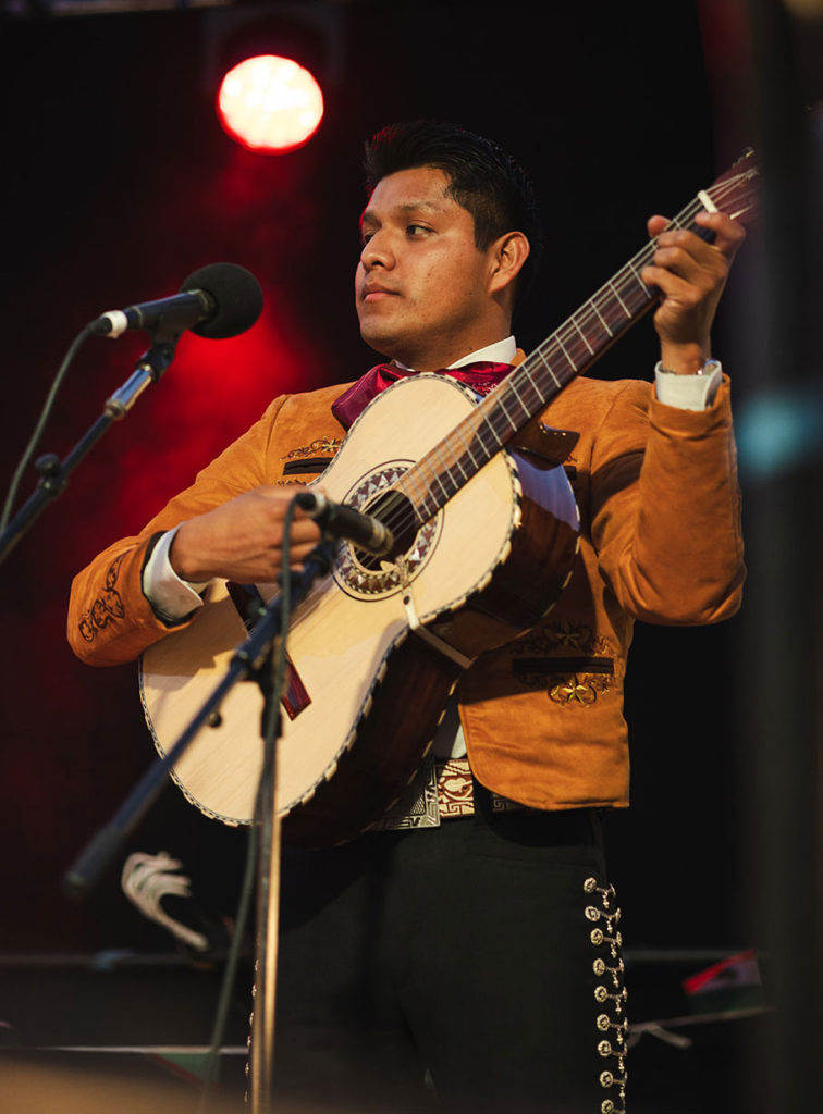 Man playing a guitar and wearing a mariachi costume onstage