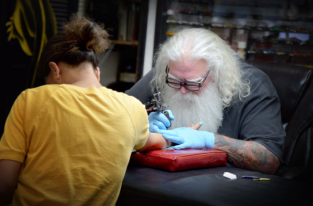 Man applying a tattoo on a woman, wearing gloves