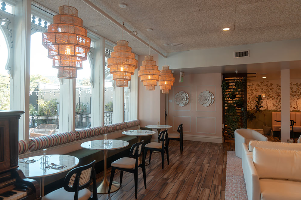 Interior of a Victorian building with small tables near a window next to couches, with decorative light fixtures hanging from the ceiling