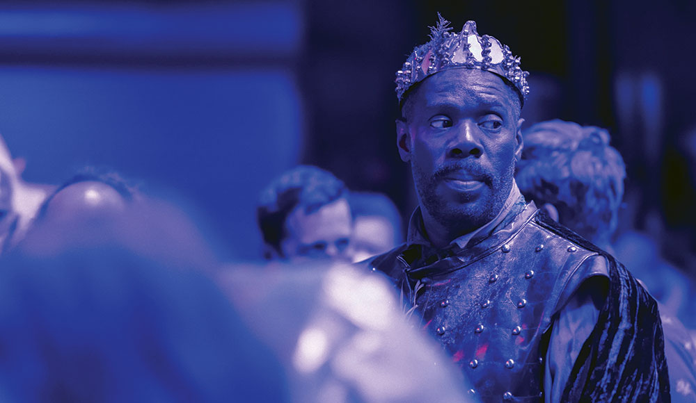 Man wearing a crown, shown in moody stage lighting