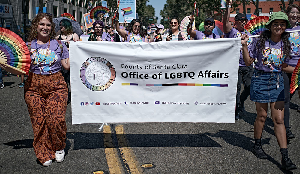 Parade with members of the Santa Clara County Office of LGBTQ Affairs marching with a banner