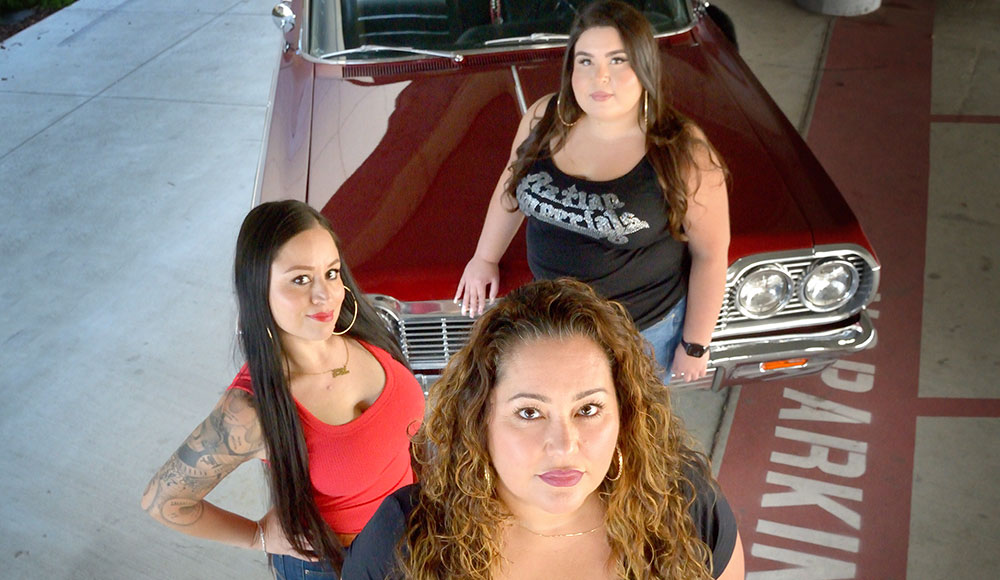 Three women standing in front of a car