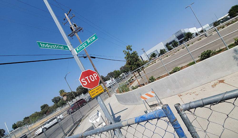 Intersection signs shot at an angle with industrial landscape around it