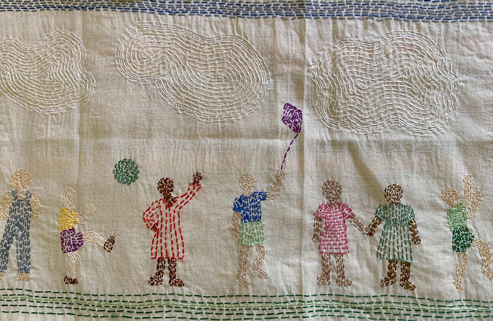 Embroidered scene of children playing outside with a ball and a kite