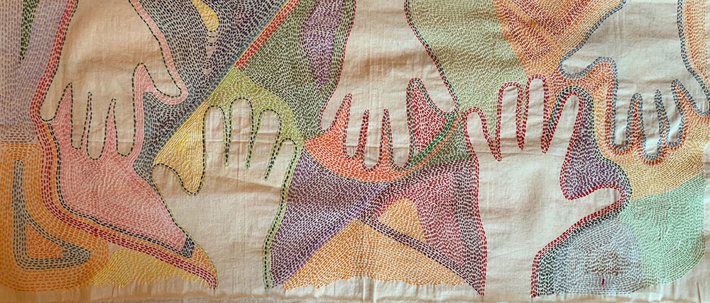 Embroidered artwork with outlines of hands against a brightly colored background