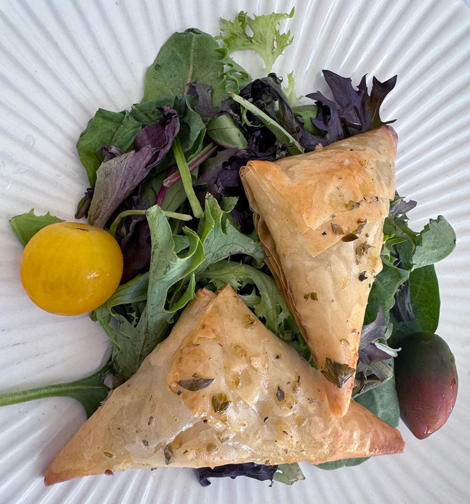 Two triangular pastries on a bed of greens and cherry tomatoes