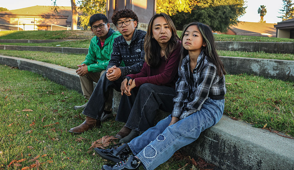 Four people sitting on a curb in front of a school