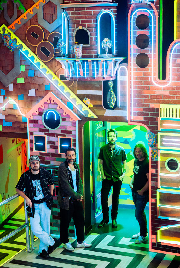 Four men against a colorful backdrop with neon lights