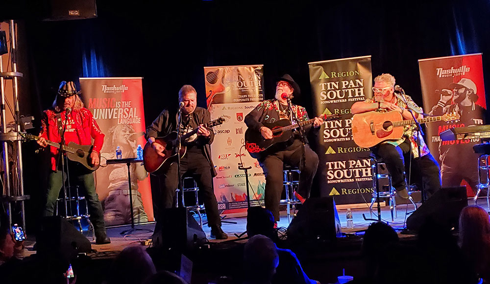 Three musicians on a stage with posters behind them