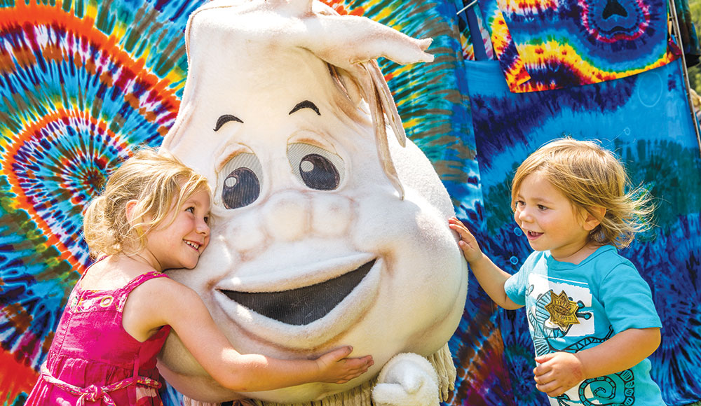 Two kids hugging a cartoon character that looks like a garlic clove