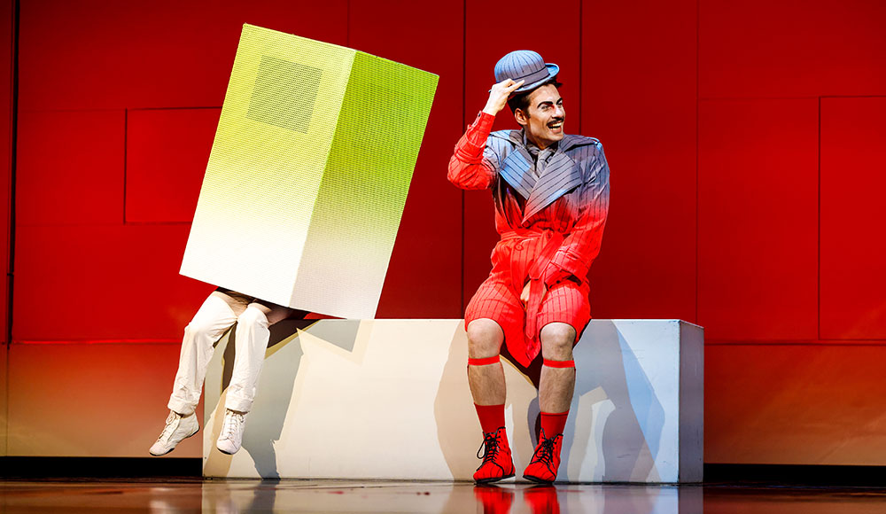 Two people on stage, one of them with a box covering thetop half of the body