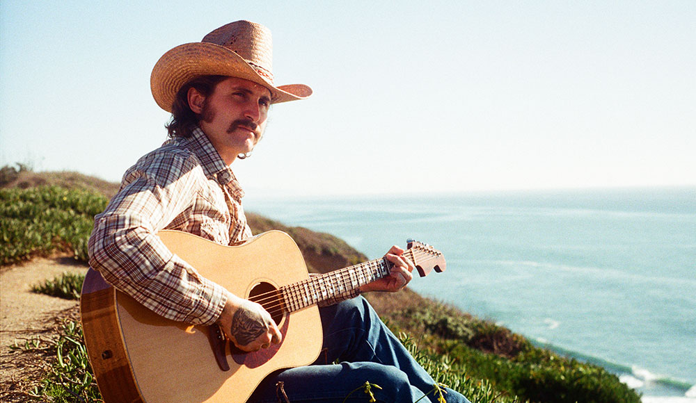 Man wearing a cowboy hat and playng guitar outside
