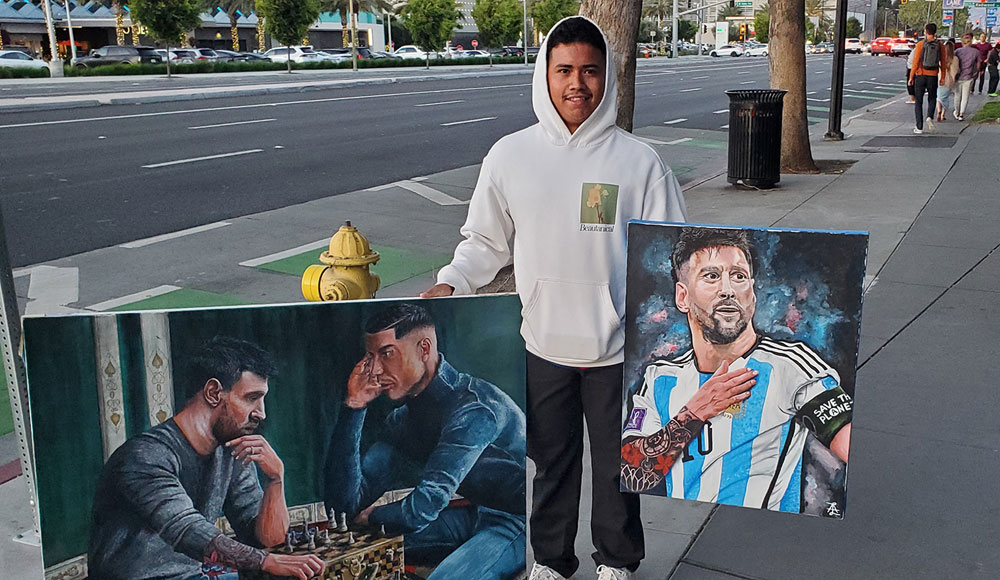 Man on the sidewalk holding up two portraits