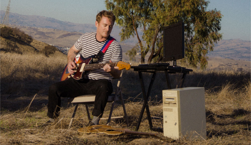Guitar player outdoors on a hillside with instruments and other equipment