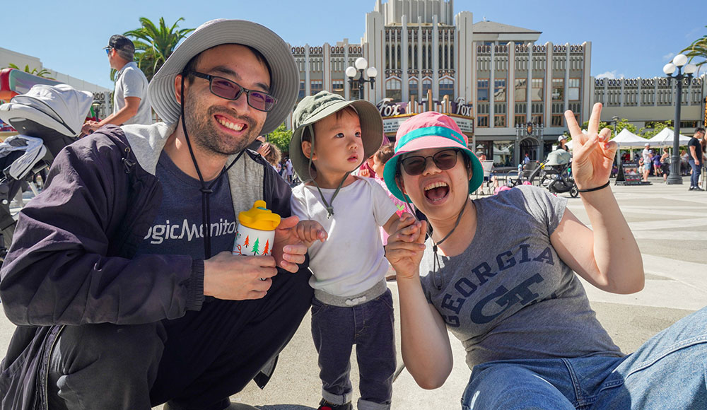 Kid and parents waving at the camera at an outdoor event