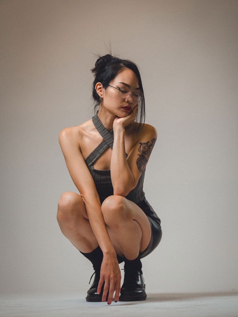 Woman crouching down against a white backdrop, wearing a dress