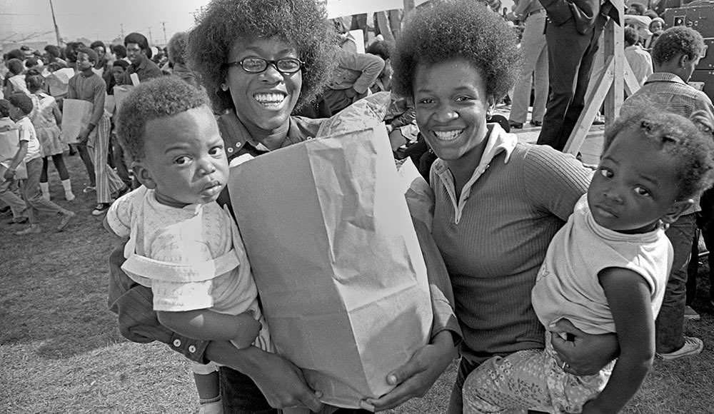 Black and white archival photo of African American families holding bags of food