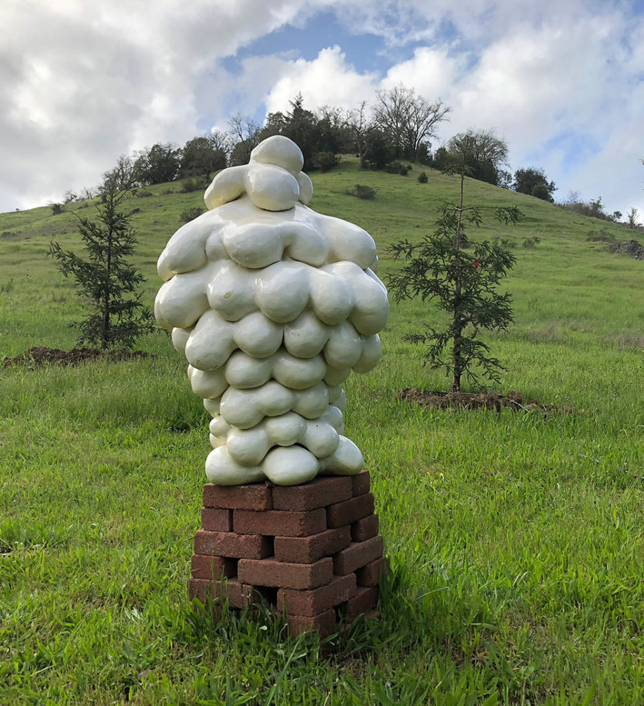 Photo of sculpture of ceramic white blobs set upon a pile of bricks on a green hillside