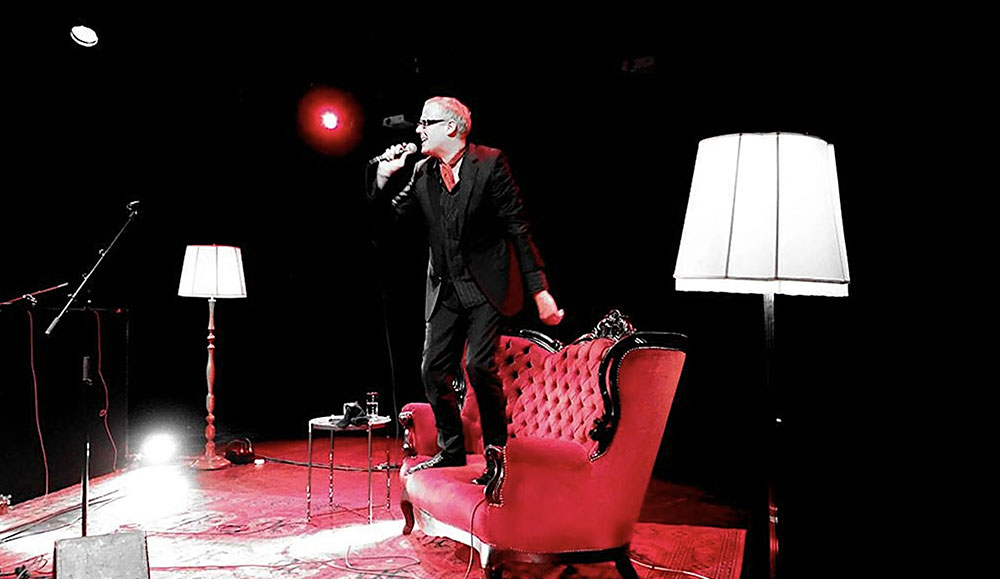 Man holding a microphone on stage while standing on an old-fashioned couch