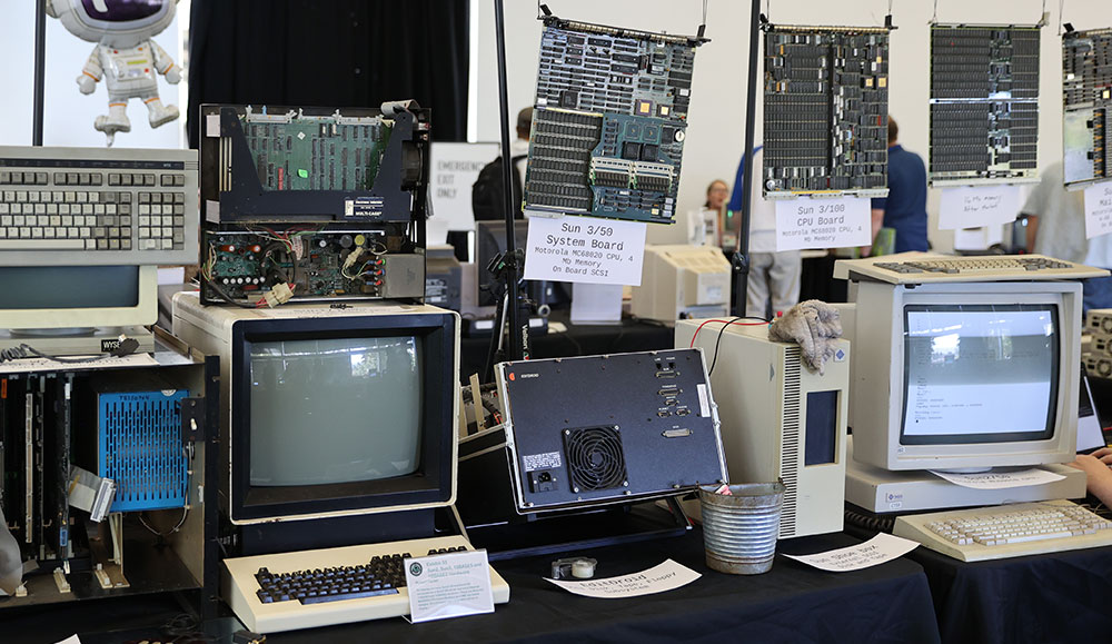 Row of old computers on a desk with motherboards hanging on a wall behind that