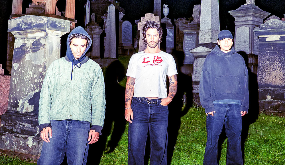 Three men standing in a cemetery surrounded by large tombstones