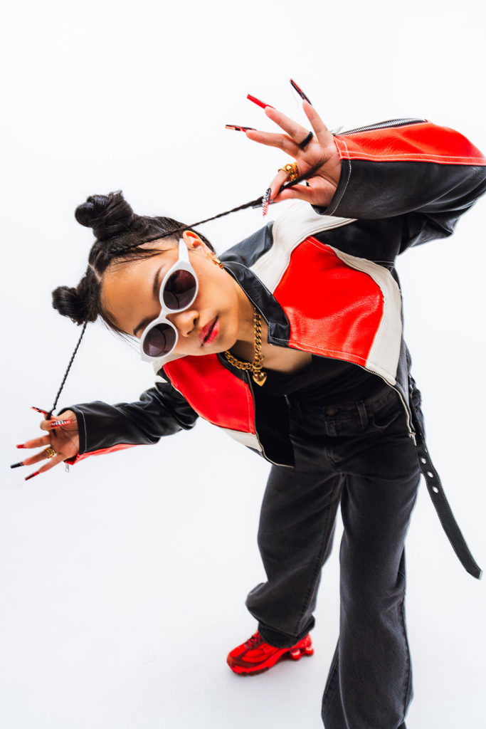 Woman looking up at the camera, wearing a black, red and white jacket with black pants and red athletic shoes