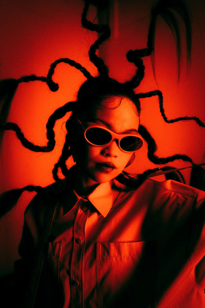 Woman shot with a dramatic red filter, her braids twisted above her head