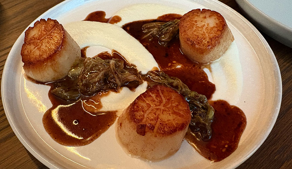 Plate of food on a table with three scallops