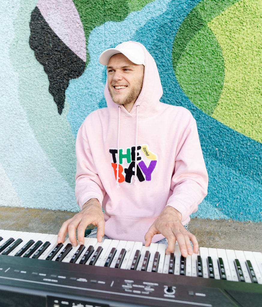 Man playing the piano outside against a wall with a mural