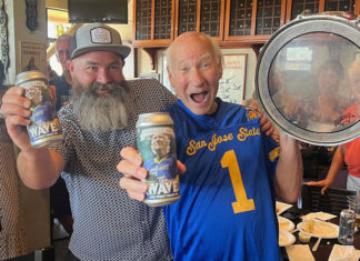 Two men holding up cans of beer, and one has a hand drum