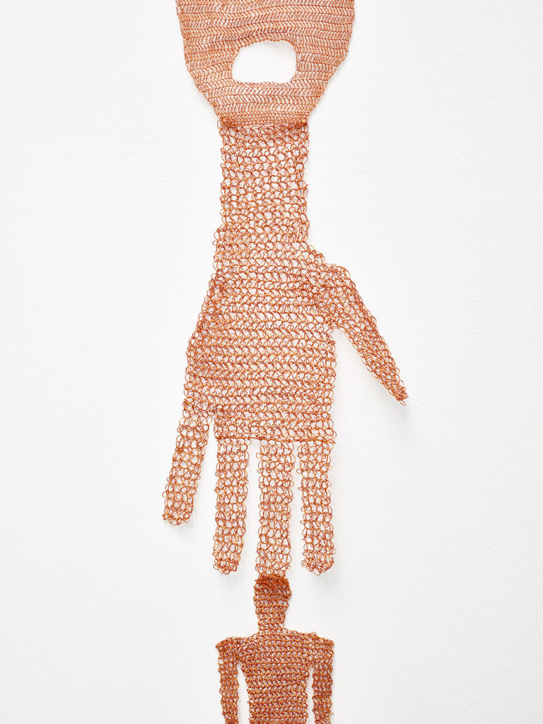 Flat sculpture of a large hand with a finger resting on the head of a small figure, crocheted out of copper