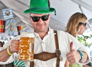 Man dressed in lederhosen holding up a beer