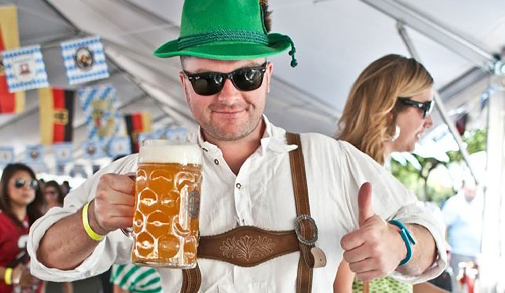 Man dressed in lederhosen holding up a beer