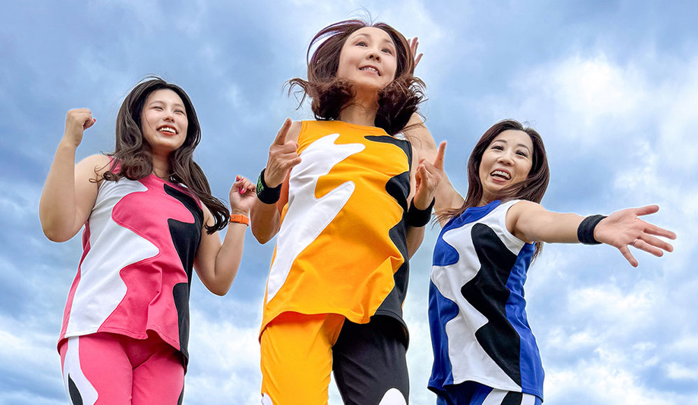 Three women wearing boldly colored pants and matching tops, jumping in the air