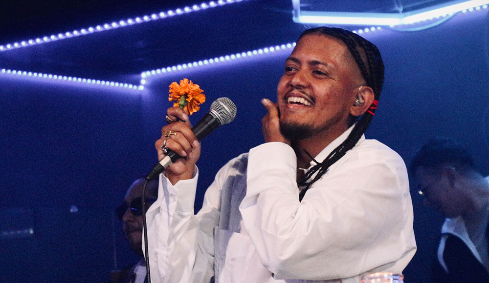 Man singing into a microphone and holding a marigold