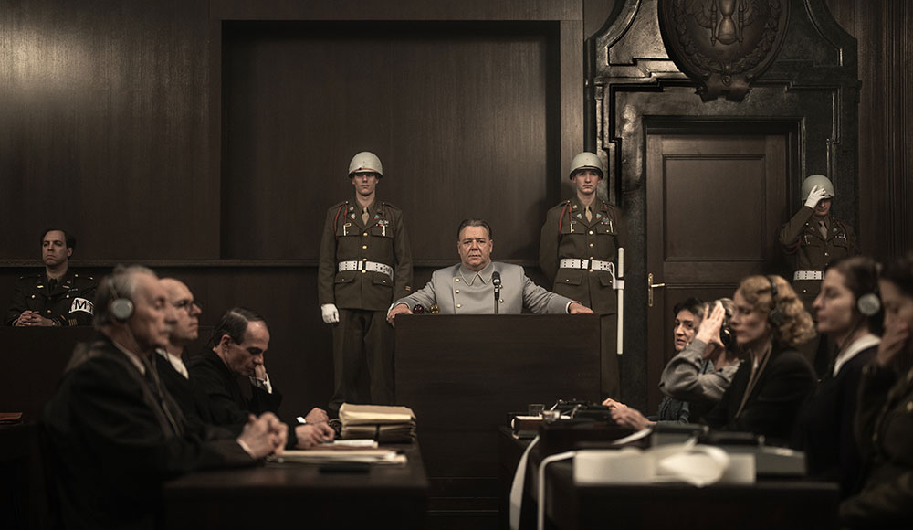 Man taking the stand, military police on either side of him, with other court personnel also in the courtroom