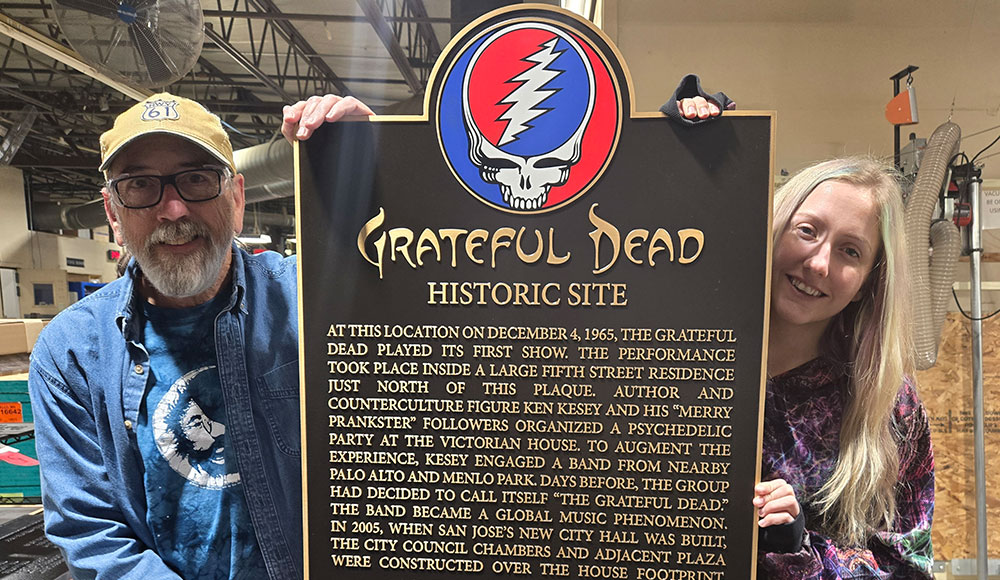 Two people on either side of a plaque, holding it upright. Plaque has the Grateful Dead’s logo on it